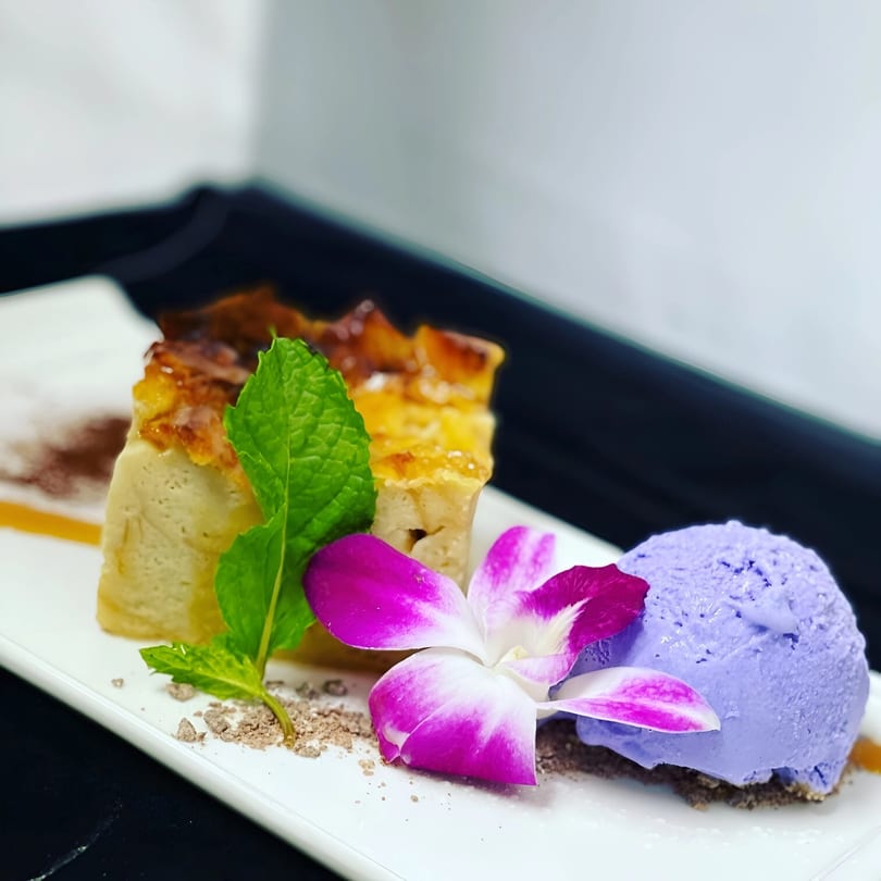 Japanese dessert with a slice of cake, purple ice cream, mint, and an orchid on a white plate.