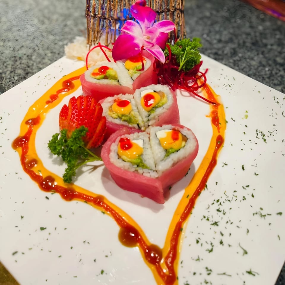 Heart-shaped sushi rolls with mango and avocado, garnished with strawberries and an orchid.