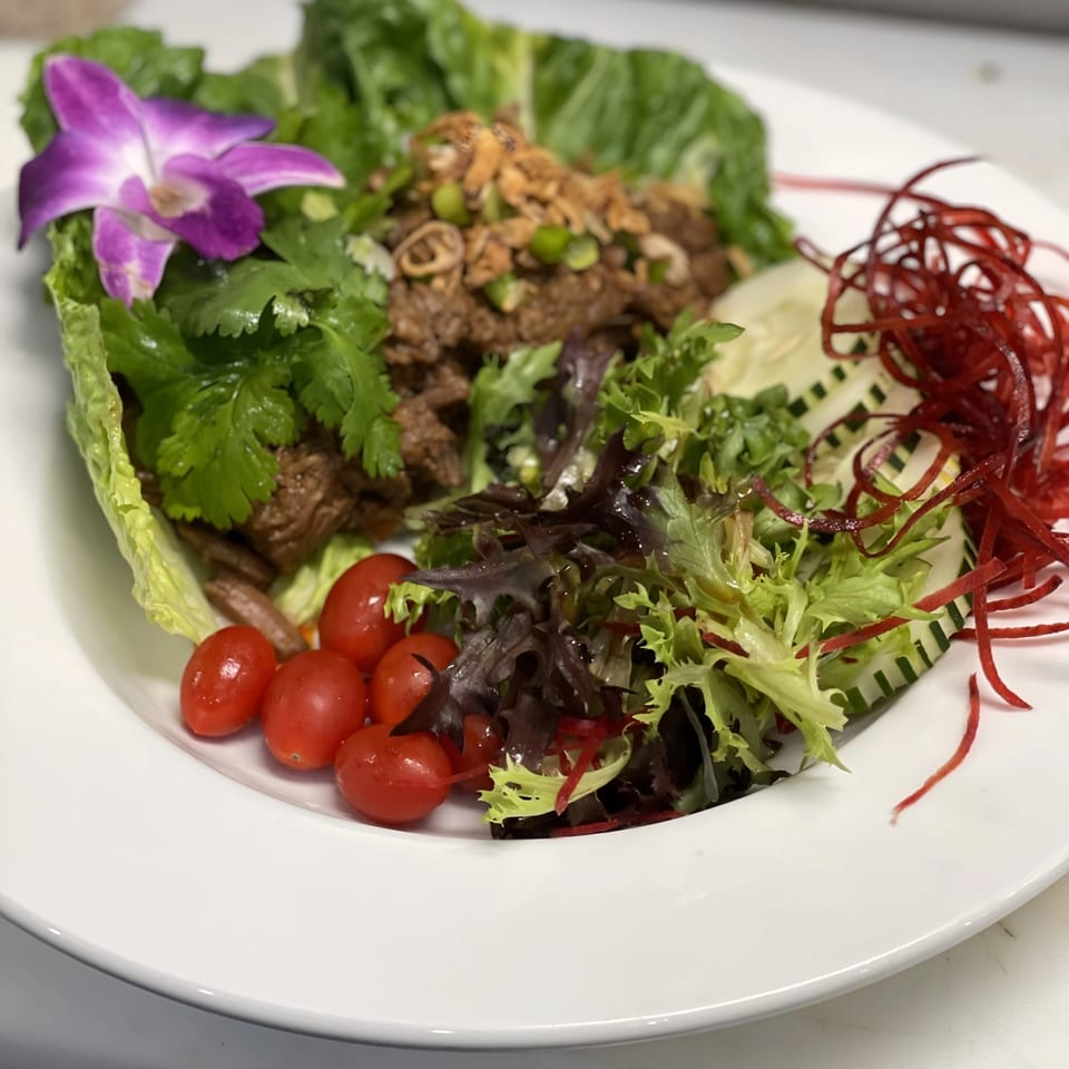 Japanese lettuce wraps with meat, cherry tomatoes, mixed greens, and a purple orchid garnish.