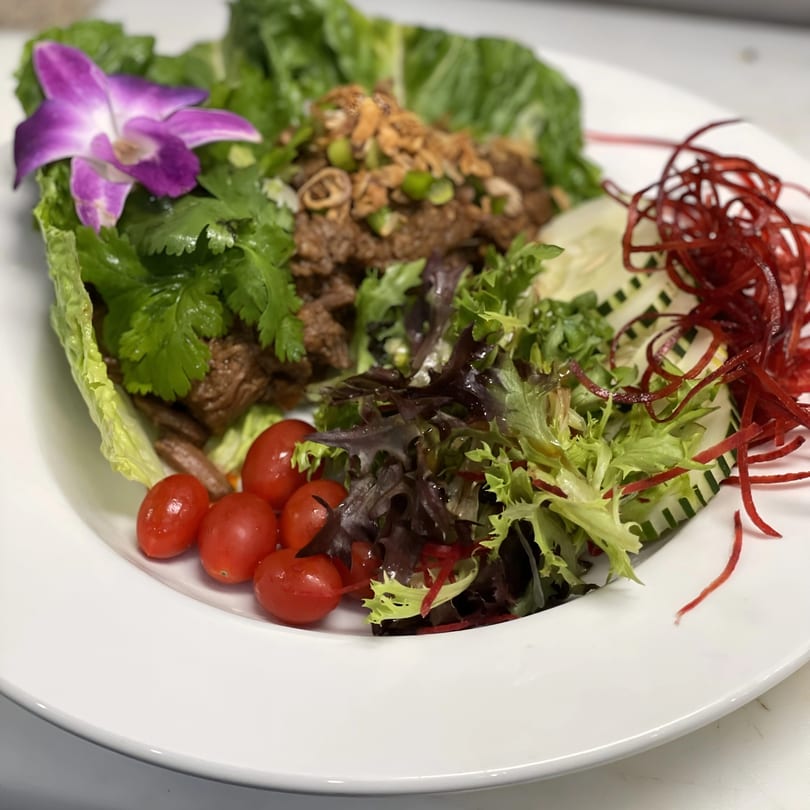 Japanese lettuce wraps with meat, cherry tomatoes, mixed greens, and a purple orchid garnish.