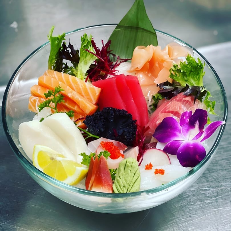A colorful sashimi bowl from Saisaki Van Wert, featuring various fish, roe, and a purple orchid.